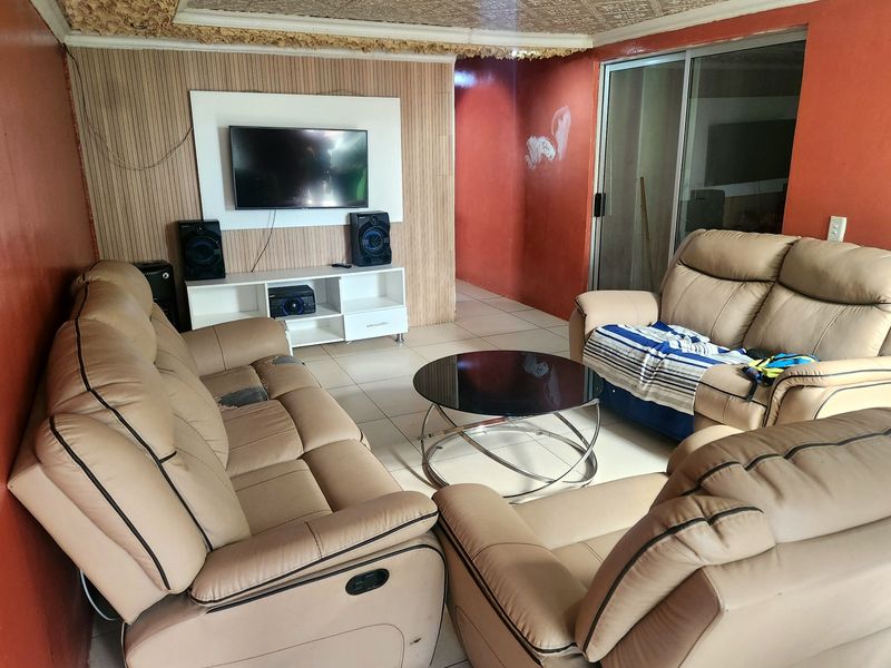 A living room featuring tiled flooring, a sliding glass door, and a wall-mounted media panel, requiring cosmetic updates to the walls and ceiling.
