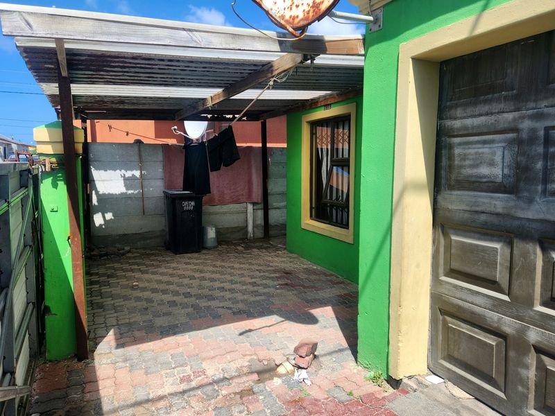 A covered outdoor patio area featuring paved flooring, a corrugated iron roof, and direct access to the garage and main building structure.