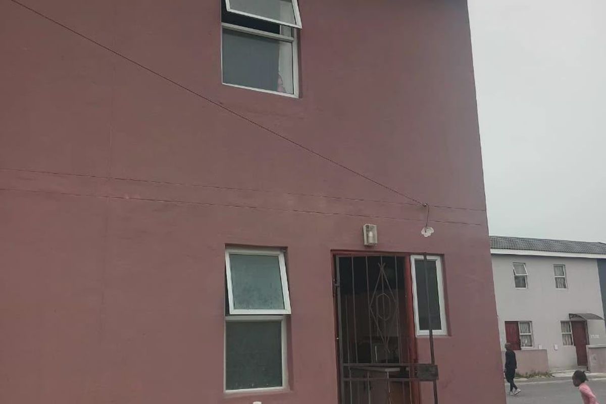 Rear exterior view of a two-story residential building featuring painted masonry walls, security gate, and casement windows.