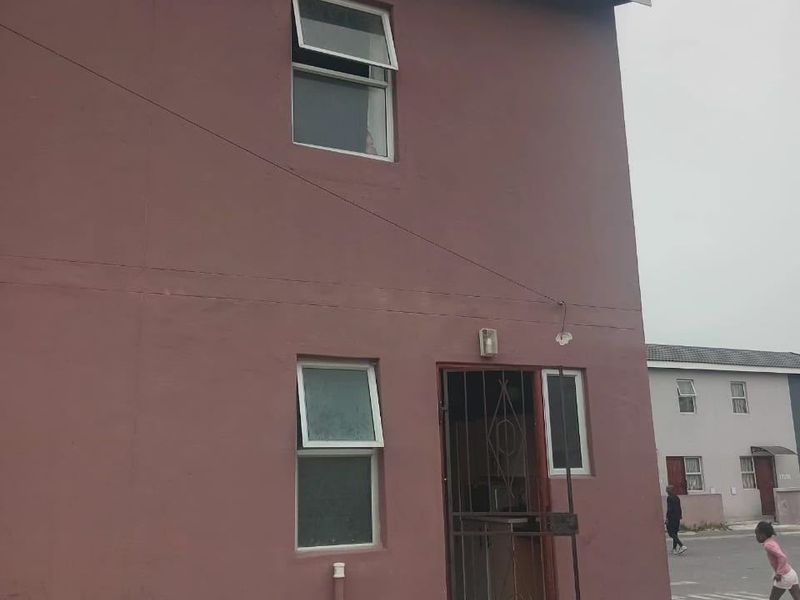 Rear exterior view of a two-story residential building featuring painted masonry walls, security gate, and casement windows.
