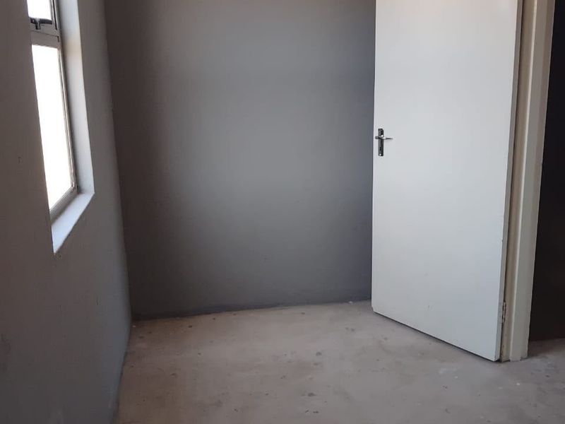An empty bedroom featuring grey painted walls, an internal door, and an unfinished concrete floor, awaiting final flooring installation.