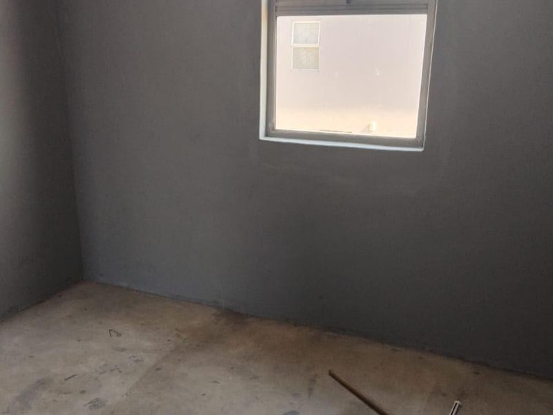 An unfinished bedroom space featuring raw plastered walls and a concrete floor, awaiting final flooring and wall finishes.