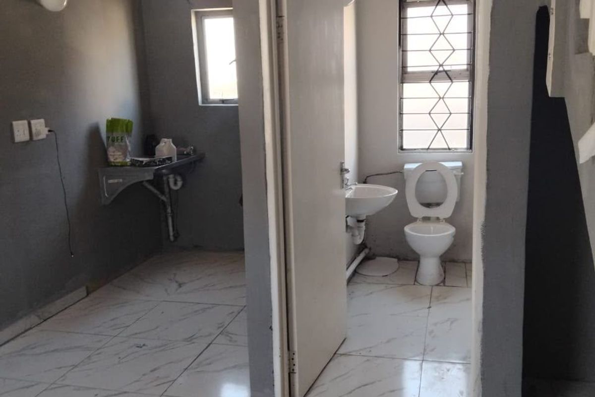 A small bathroom featuring a pedestal basin and toilet with marble-look floor tiles, currently requiring finishing touches to the walls and door frame.