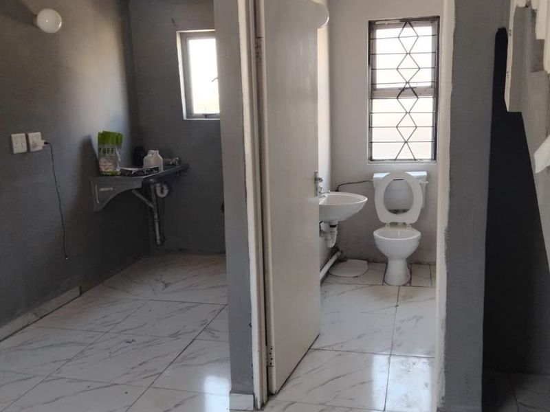 A small bathroom featuring a pedestal basin and toilet with marble-look floor tiles, currently requiring finishing touches to the walls and door frame.