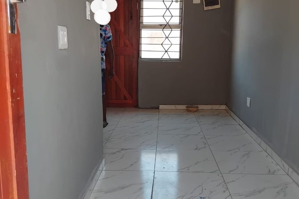 An empty living area featuring white marble-look floor tiles, grey walls, and a timber entrance door with security gate.
