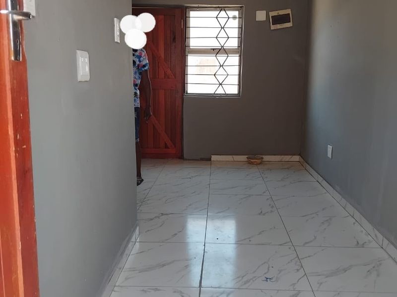 An empty living area featuring white marble-look floor tiles, grey walls, and a timber entrance door with security gate.