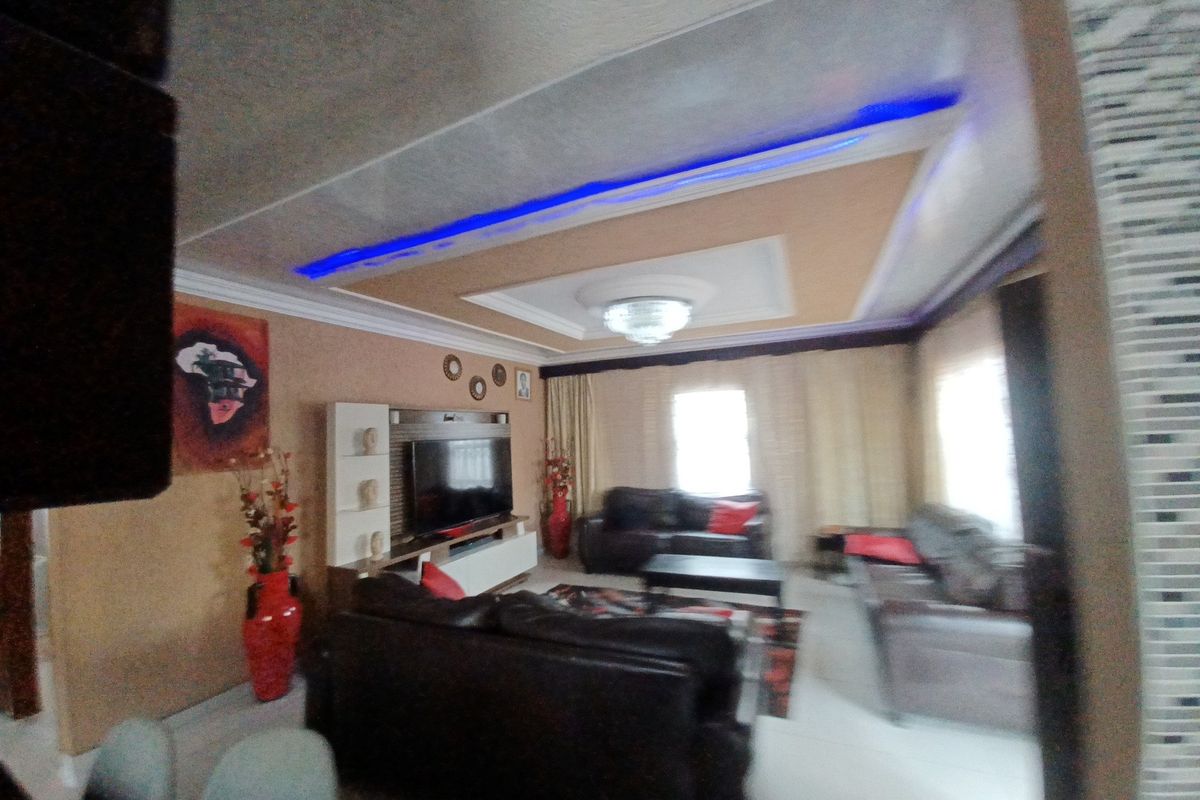 A living room featuring a recessed ceiling with integrated LED lighting, a central chandelier, and a built-in media unit.