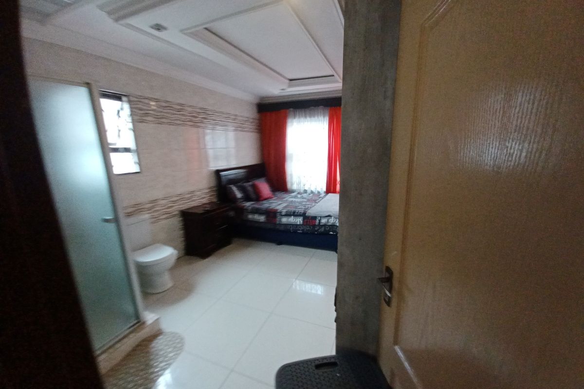 A bedroom featuring tiled flooring, a tray ceiling, and an integrated en-suite bathroom with a shower and toilet.
