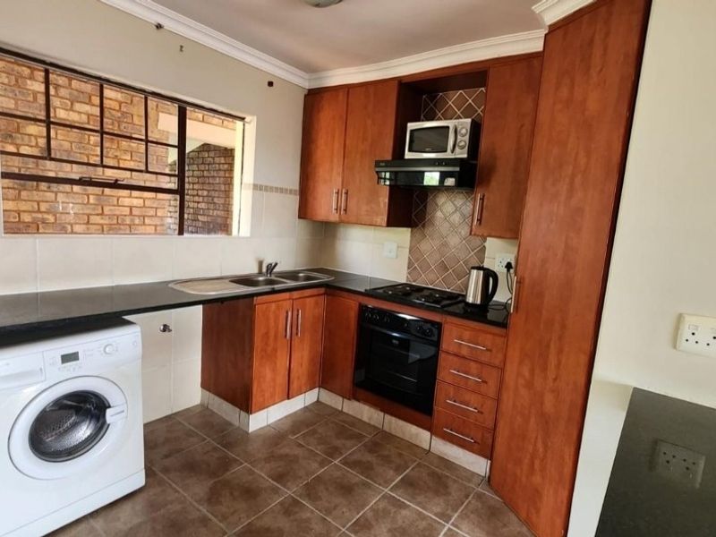 Functional kitchen featuring wood-look cabinetry, dark countertops, built-in oven and hob, and integrated laundry plumbing, offering a practical layout for daily use.