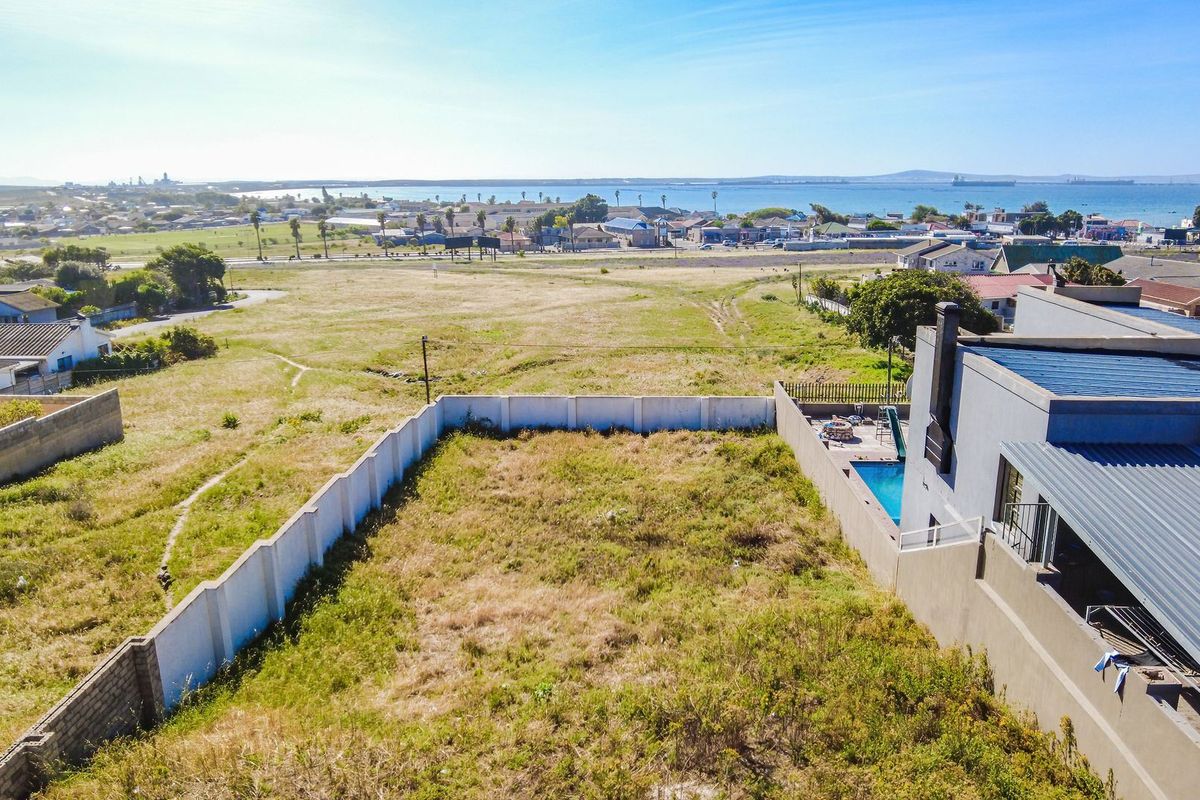 Aerial view of a vacant residential plot featuring a boundary wall and an adjacent property with a swimming pool, overlooking the coastal landscape.