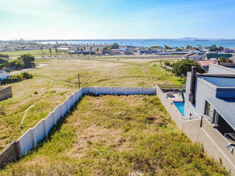 Aerial view of a vacant residential plot featuring a boundary wall and an adjacent property with a swimming pool, overlooking the coastal landscape.