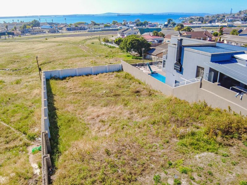 An aerial view of a vacant residential plot featuring boundary walls, situated in a developed neighborhood with coastal views.