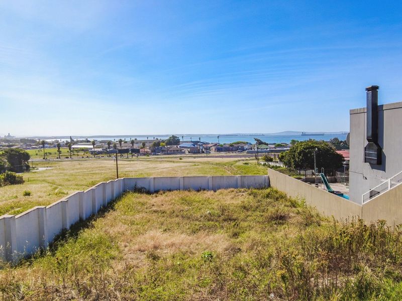 Elevated view overlooking a vacant residential plot with perimeter boundary walls and distant coastal landscape.