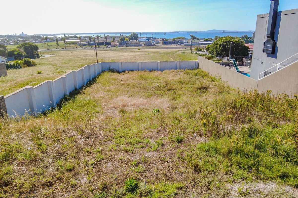 An elevated view of a vacant residential plot featuring perimeter boundary walls and distant coastal views.