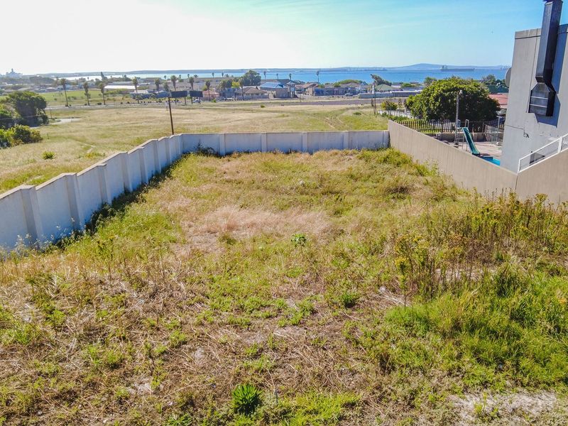 An elevated view of a vacant residential plot featuring perimeter boundary walls and distant coastal views.