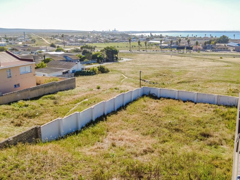 Aerial view of a vacant residential plot featuring a perimeter wall, situated in a coastal neighborhood with surrounding residential development.