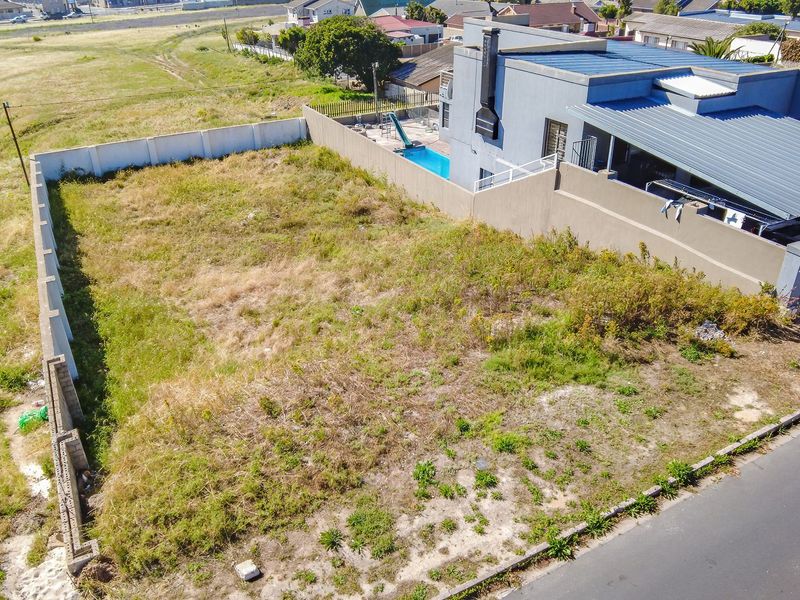 Aerial view of a vacant residential plot featuring perimeter boundary walls and direct road access, situated in an established neighborhood.