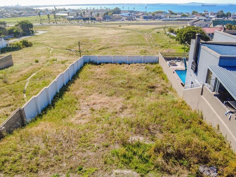 Aerial view of a vacant residential plot featuring boundary walls, situated in a coastal neighborhood with surrounding landscape views.