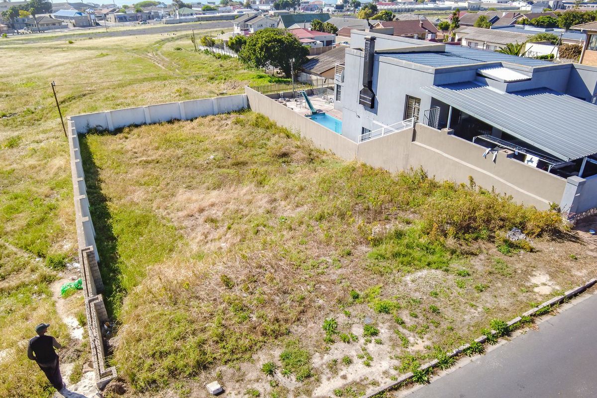 Aerial view of a vacant residential plot featuring perimeter walling and direct street access, situated in a developed suburban neighborhood.