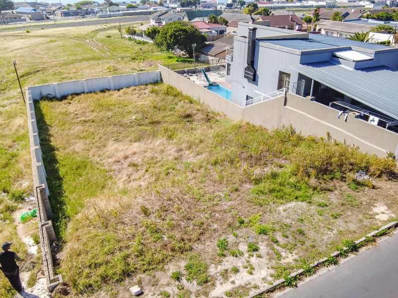 Aerial view of a vacant residential plot featuring perimeter walling and direct street access, situated in a developed suburban neighborhood.