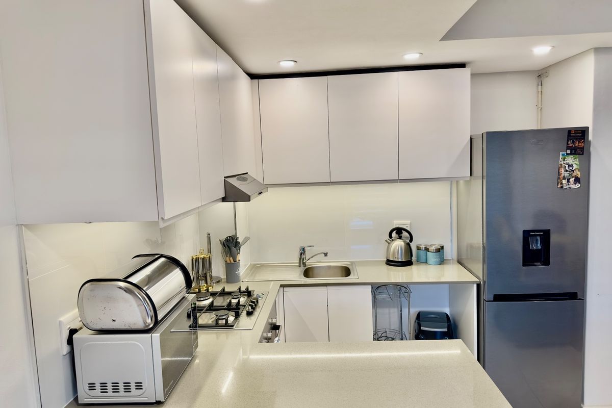 Modern kitchen featuring white cabinetry, stone countertops, a gas hob, and integrated lighting, offering a clean and functional workspace.