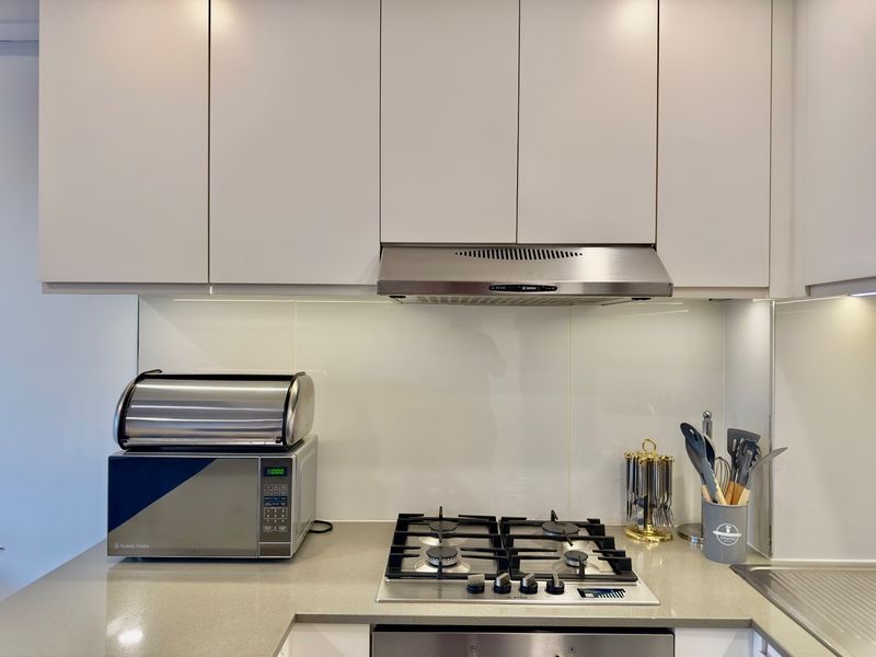 Modern kitchen featuring a gas cooktop, stainless steel extractor fan, stone countertops, and sleek white cabinetry with integrated lighting.