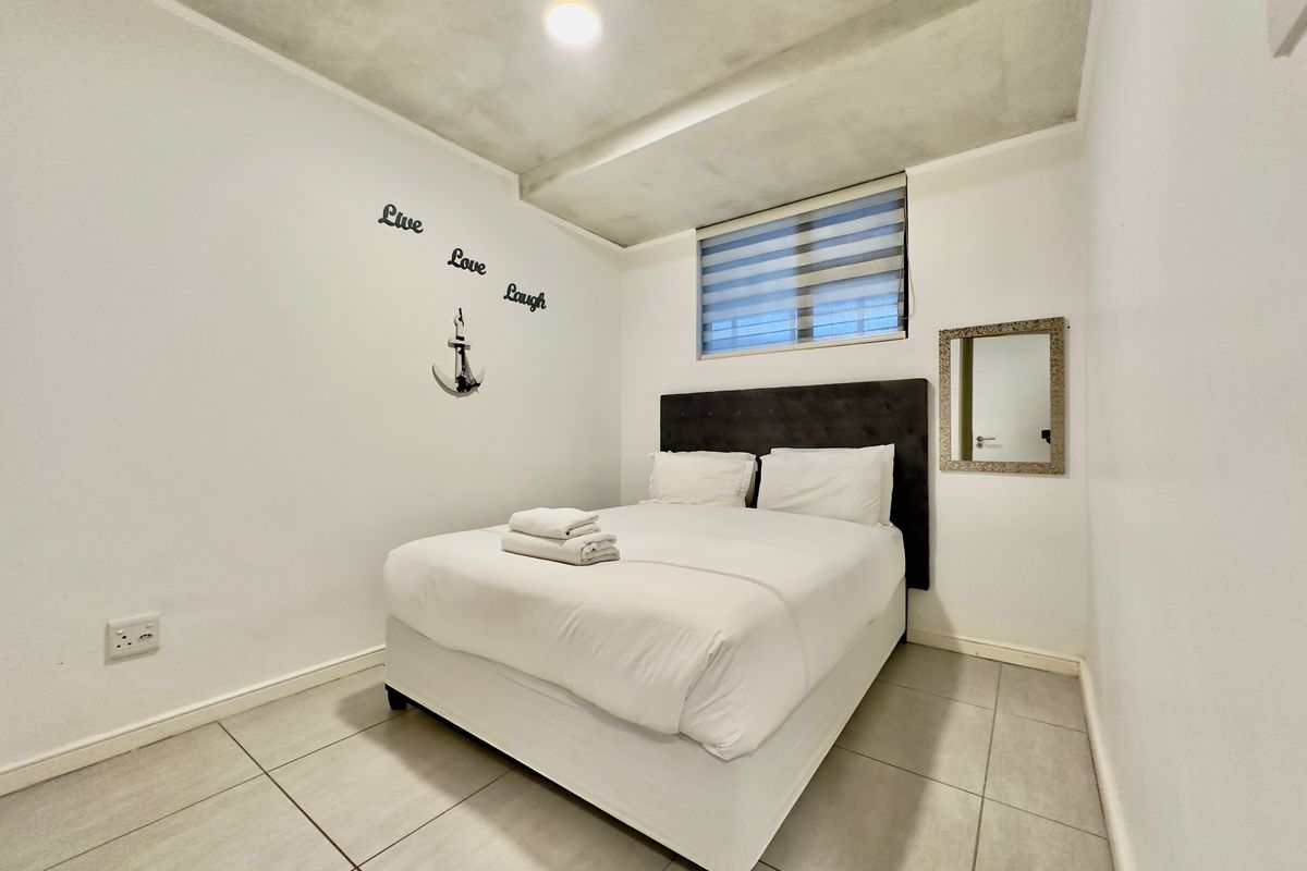 A compact bedroom featuring neutral tiled flooring, a modern day-night roller blind, and recessed ceiling lighting, providing a clean and functional sleeping space.