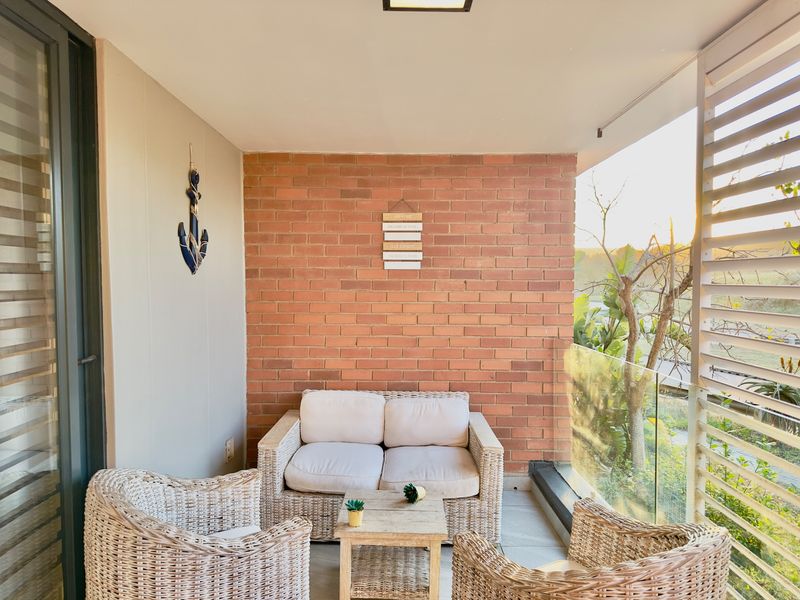 A covered balcony featuring an exposed brick feature wall, glass balustrade, and tiled flooring, offering a pleasant outdoor space for relaxation.