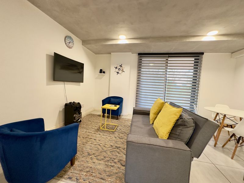 A well-lit living room featuring modern tiled flooring, recessed ceiling lights, and adjustable roller blinds for privacy.