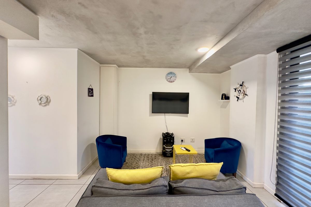 A well-lit living room featuring tiled flooring, a textured ceiling finish, and modern roller blinds, providing a clean and functional space.