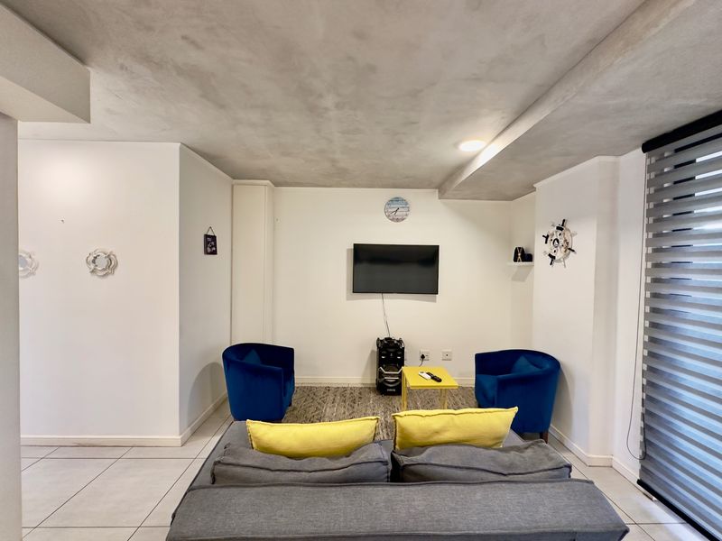 A well-lit living room featuring tiled flooring, a textured ceiling finish, and modern roller blinds, providing a clean and functional space.