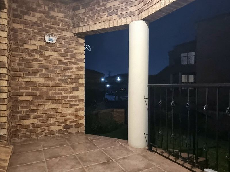 A covered balcony featuring brick walls, tiled flooring, and a metal balustrade, offering an outdoor space for relaxation.