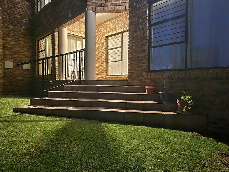Night view of a face brick apartment exterior featuring a tiled patio entrance with wrought iron railings and security-fitted windows overlooking a lawn.