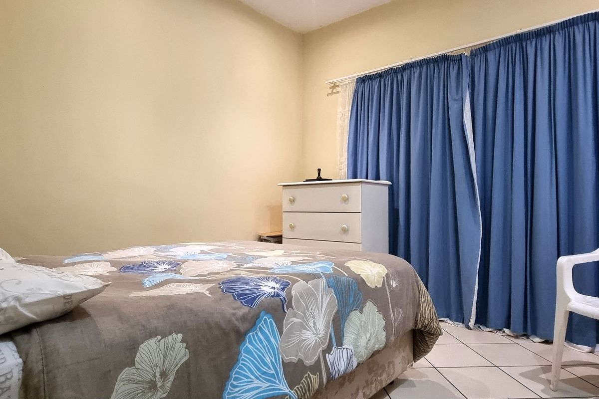 A functional bedroom featuring tiled flooring and large window curtains, offering a neutral space ready for personalization.