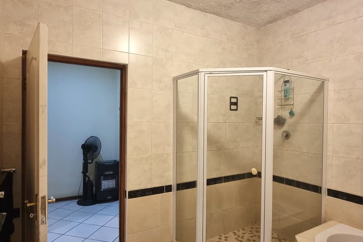A functional bathroom featuring a corner shower enclosure, tiled walls, and a built-in bathtub, offering a practical layout for daily use.