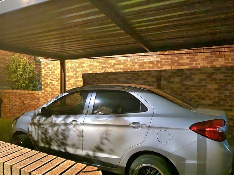 A covered carport area featuring a sturdy metal roof structure and brick boundary walls, providing secure off-street parking.