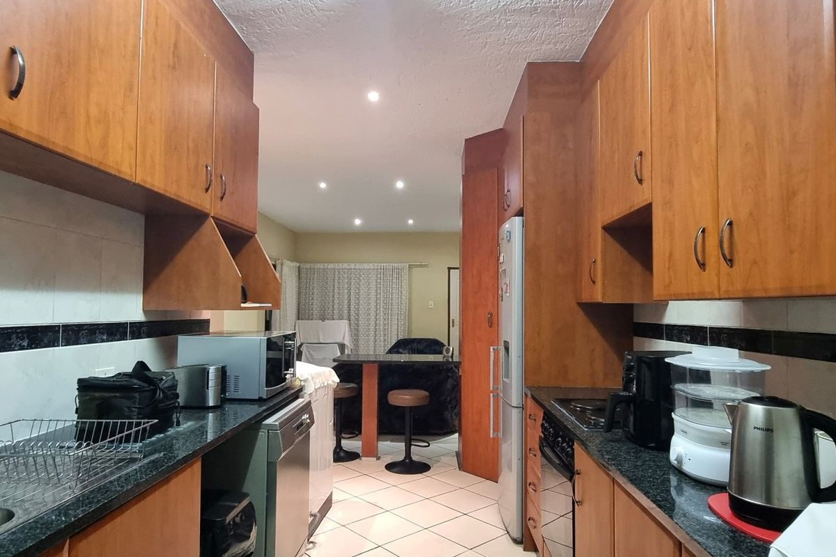 A functional galley-style kitchen featuring wood-finish cabinetry, granite countertops, tiled backsplash, and integrated appliances, leading into an open-plan living area.
