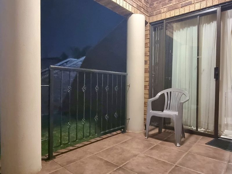 A covered patio area featuring tiled flooring, brick walls, and a metal balustrade, providing direct access to the interior living space via sliding glass doors.