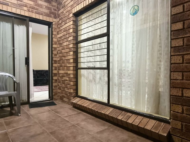 A covered patio area featuring exposed brick walls, tiled flooring, and access to the interior through a sliding glass door.
