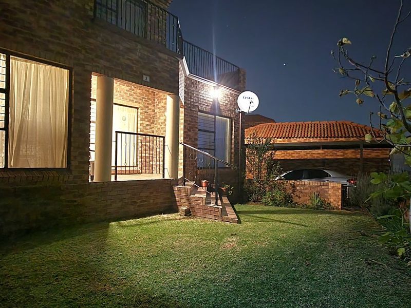 Night view of the rear exterior featuring a brick facade, a small lawn, and a balcony with metal railings.