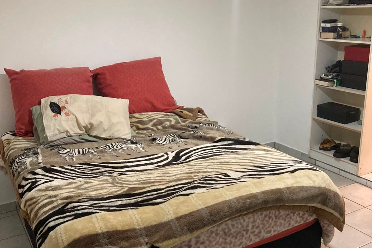 A functional bedroom featuring tiled flooring, a ceiling fan, and a built-in shelving unit for storage.