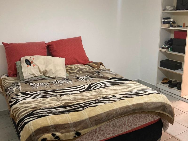 A functional bedroom featuring tiled flooring, a ceiling fan, and a built-in shelving unit for storage.