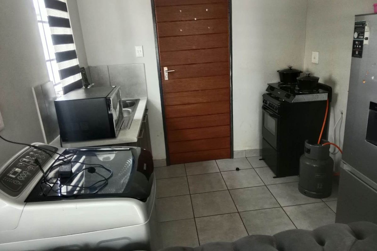 A functional kitchen area featuring tiled flooring, a gas stove with extractor, and a built-in sink, providing essential utility space.