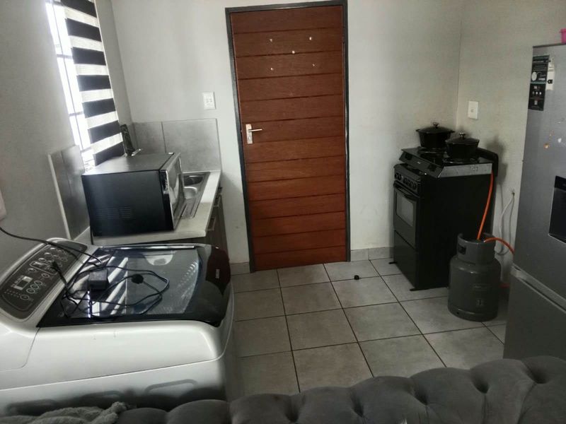A functional kitchen area featuring tiled flooring, a gas stove with extractor, and a built-in sink, providing essential utility space.