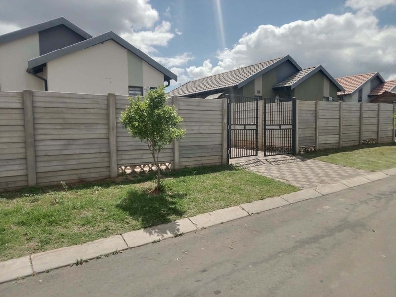 Front view of a residential property featuring a secure precast concrete boundary wall, metal pedestrian gate, and a paved driveway entrance.