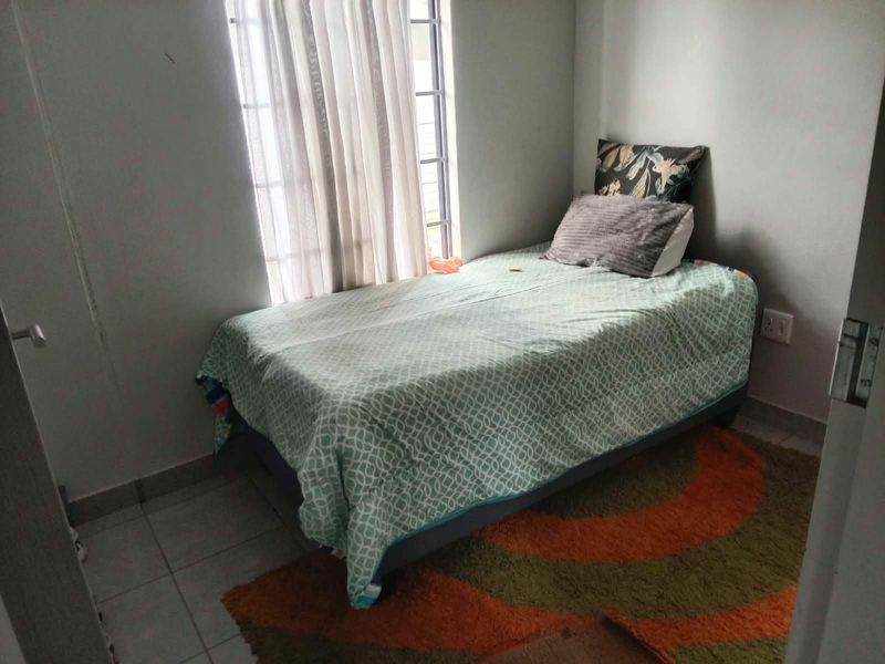 A compact bedroom featuring tiled flooring and a window with security bars, providing a functional and simple living space.