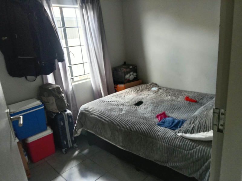 A compact bedroom featuring tiled flooring and a window with security burglar bars.