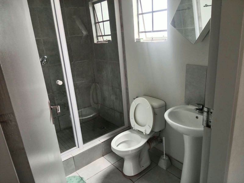 A functional bathroom featuring a shower enclosure, pedestal basin, and toilet with tiled flooring and natural light from two windows.