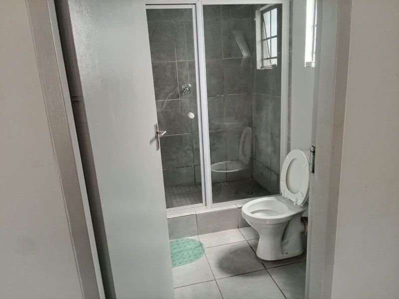 A functional bathroom featuring a glass-enclosed shower, tiled walls and flooring, and a standard toilet.