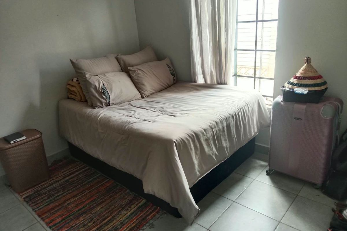 A functional bedroom featuring tiled flooring and a window fitted with security bars, providing natural light.